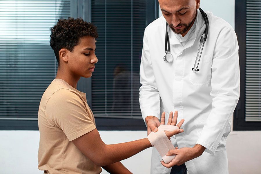 Doctor wrapping a boy’s wrist in a clinic exam room