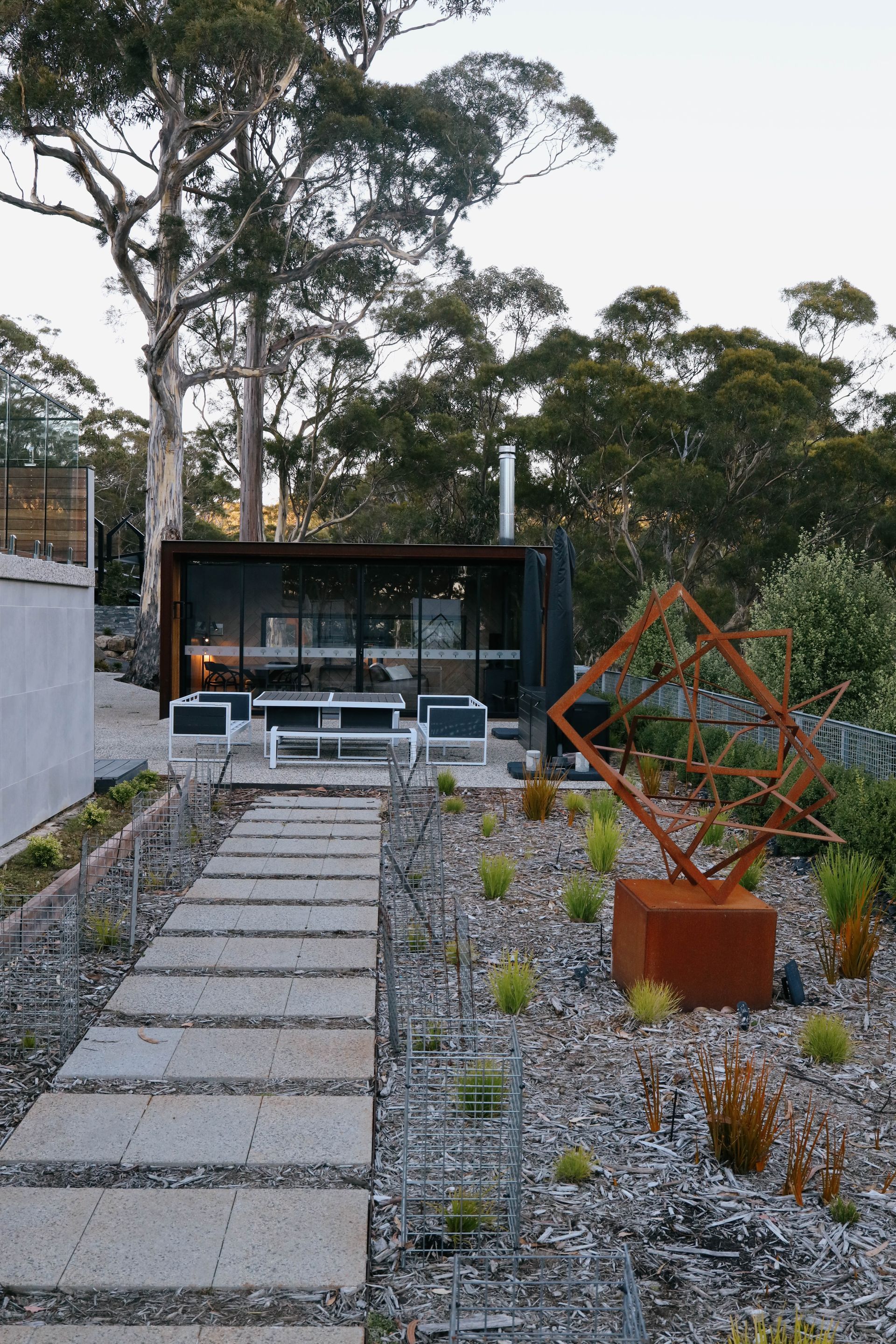 A concrete walkway leading to a house with a sculpture in the foreground.