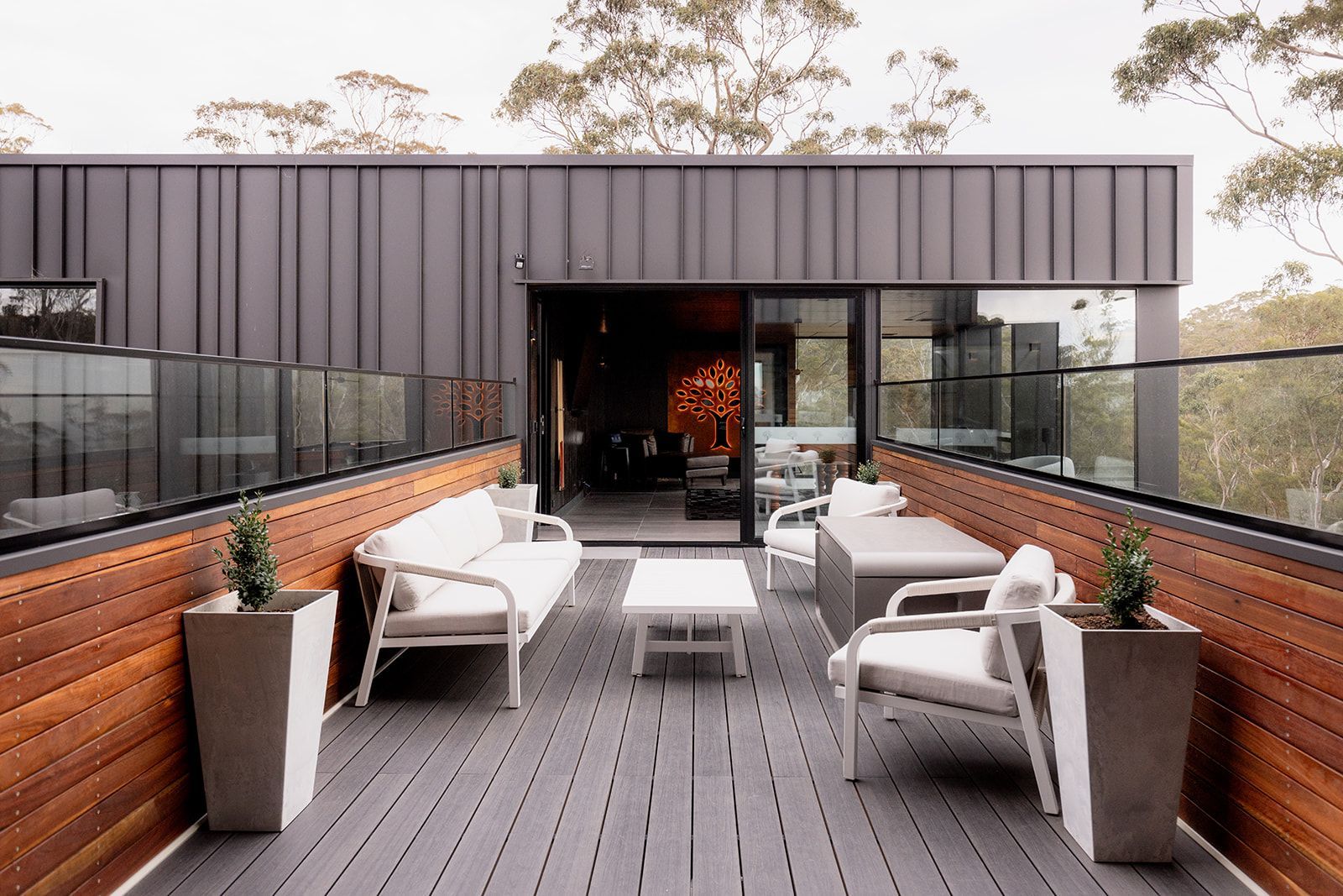 A rooftop deck with a couch , chairs , table and potted plants.