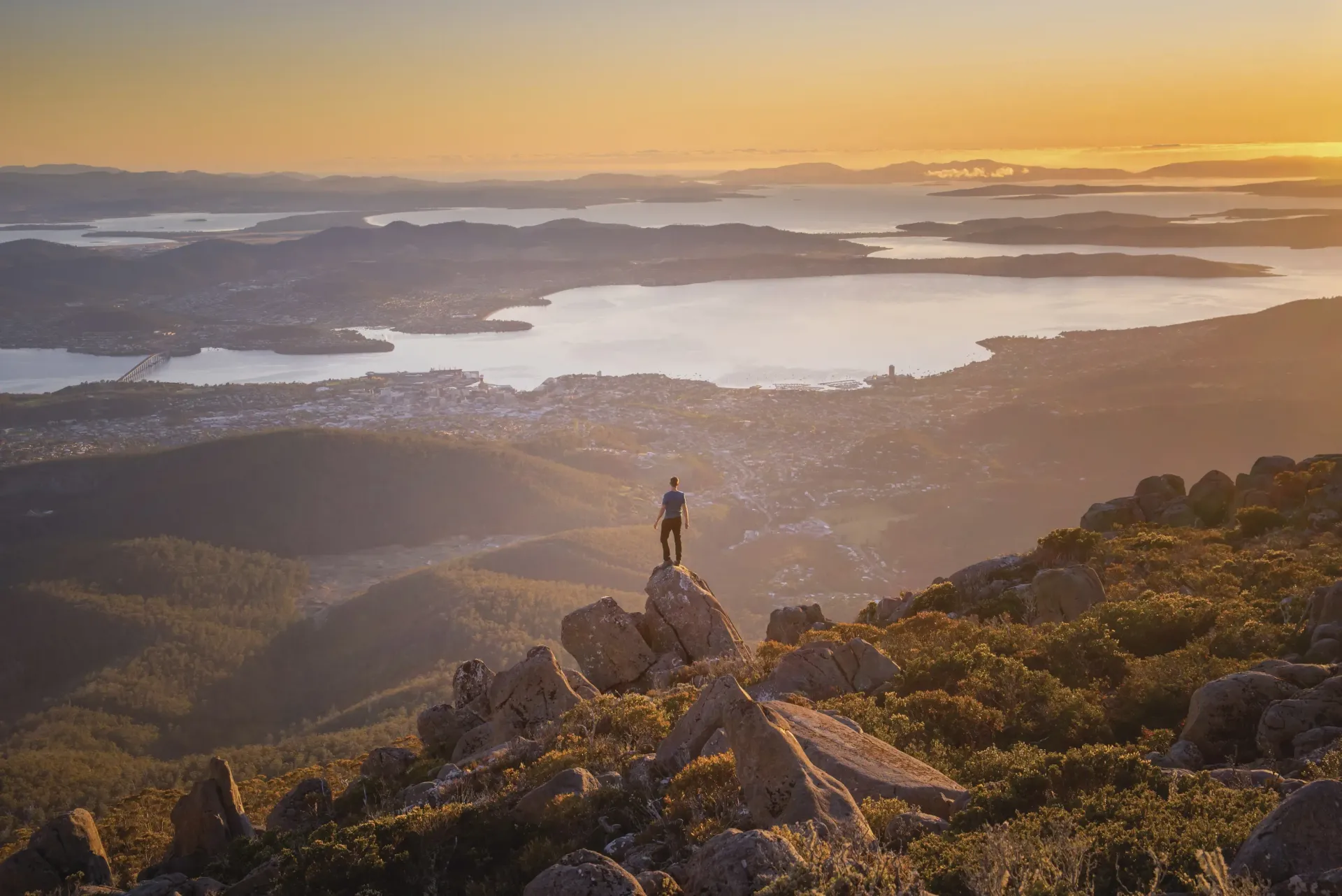 A man is standing on top of a mountain overlooking a lake.