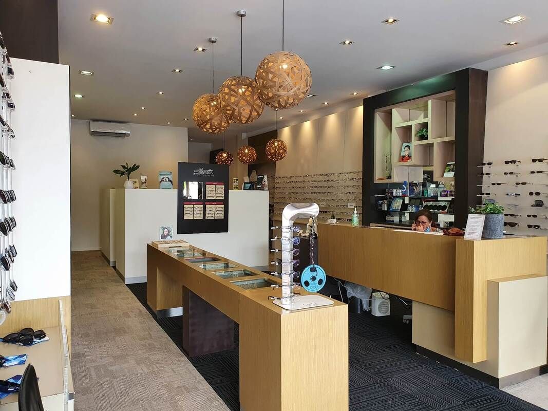 Interior view of an eye care center with wooden counters, spherical light fixtures, and eyewear displays on the walls.
