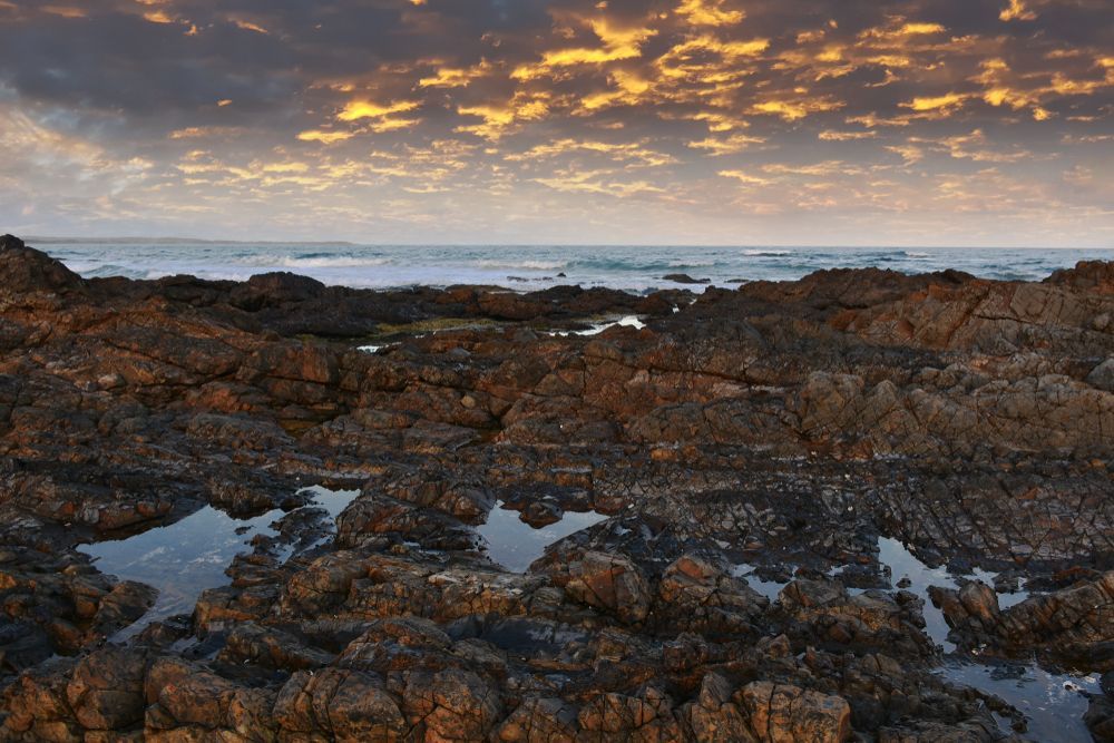 A Rocky Shoreline With a Sunset in the Background — Glen Lamberts Wall Cladding & Home Improvements in Diamond Beach, NSW