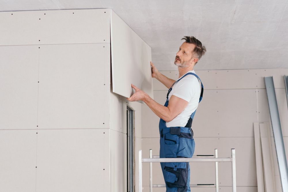 A Man is Standing on a Ladder Installing Drywall on a Wall — Glen Lamberts Wall Cladding & Home Improvements in Forster, NSW