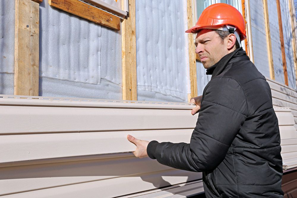 A Man Wearing a Hard Hat Is Installing Siding on A House — Glen Lamberts Wall Cladding & Home Improvements in Pampoolah, NSW