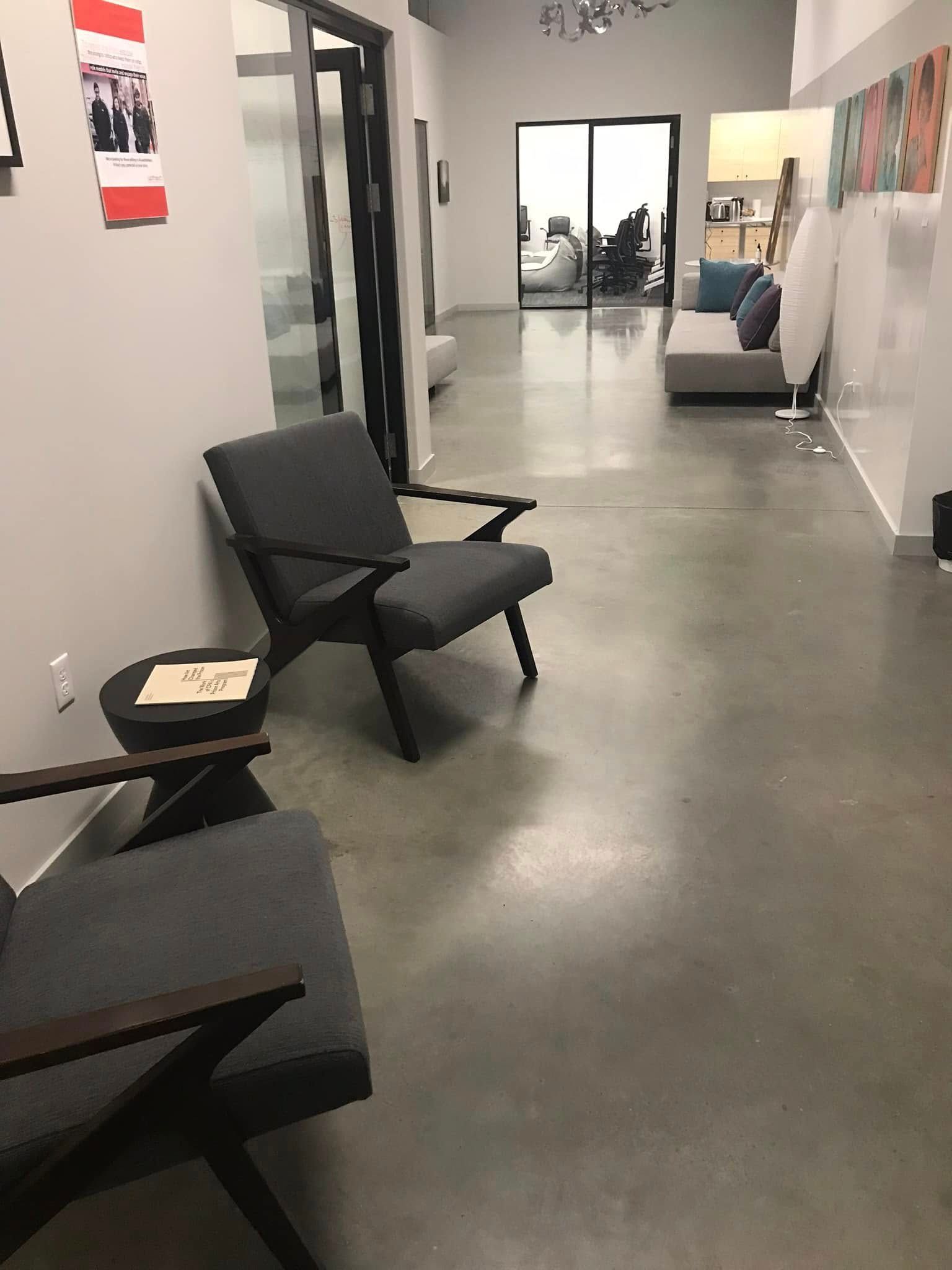 Waiting area with gray chairs, a side table, and a long hallway leading to an office space.