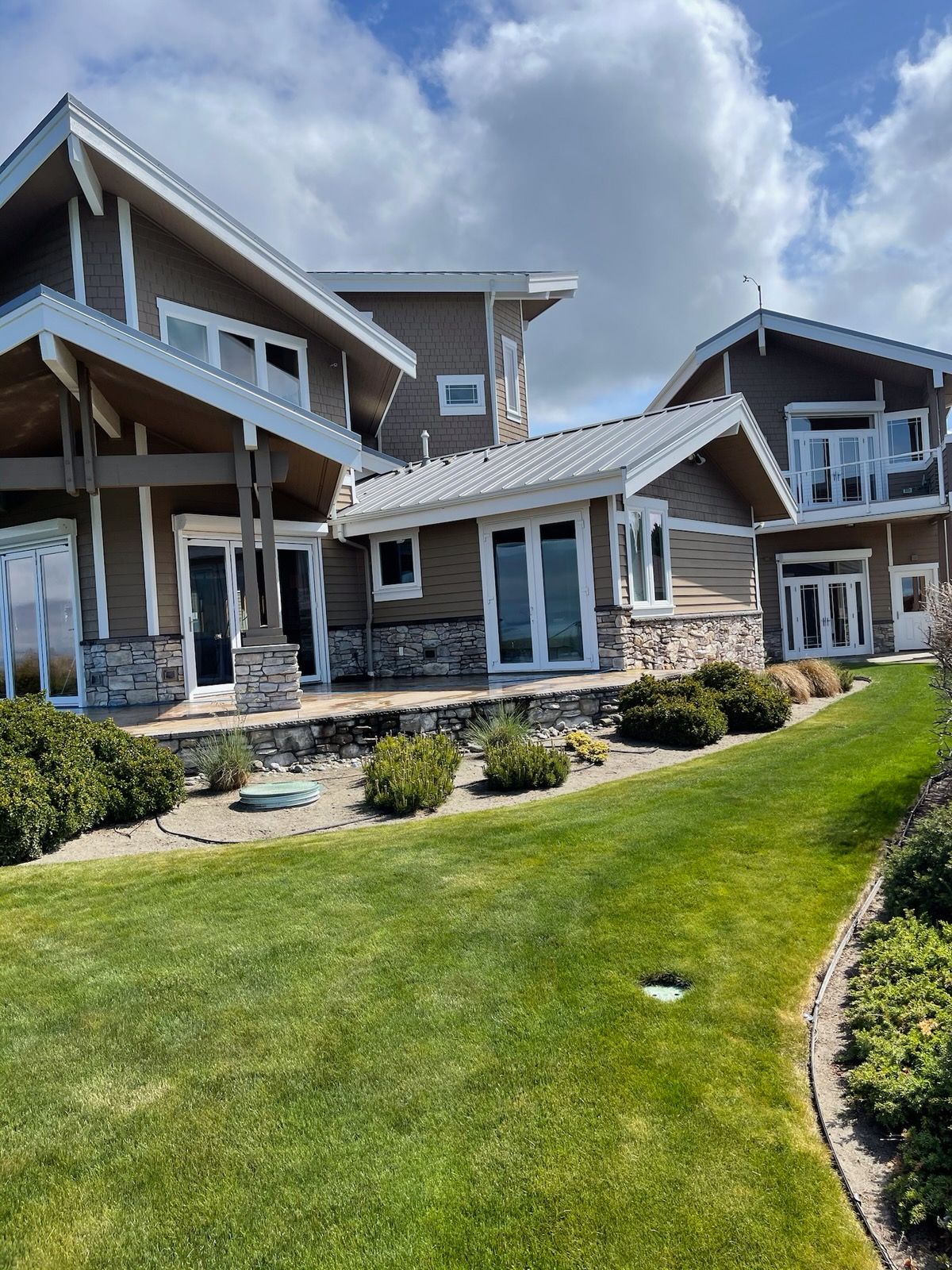 A multi-level brown house with white trim, a green lawn, and a cloudy blue sky.