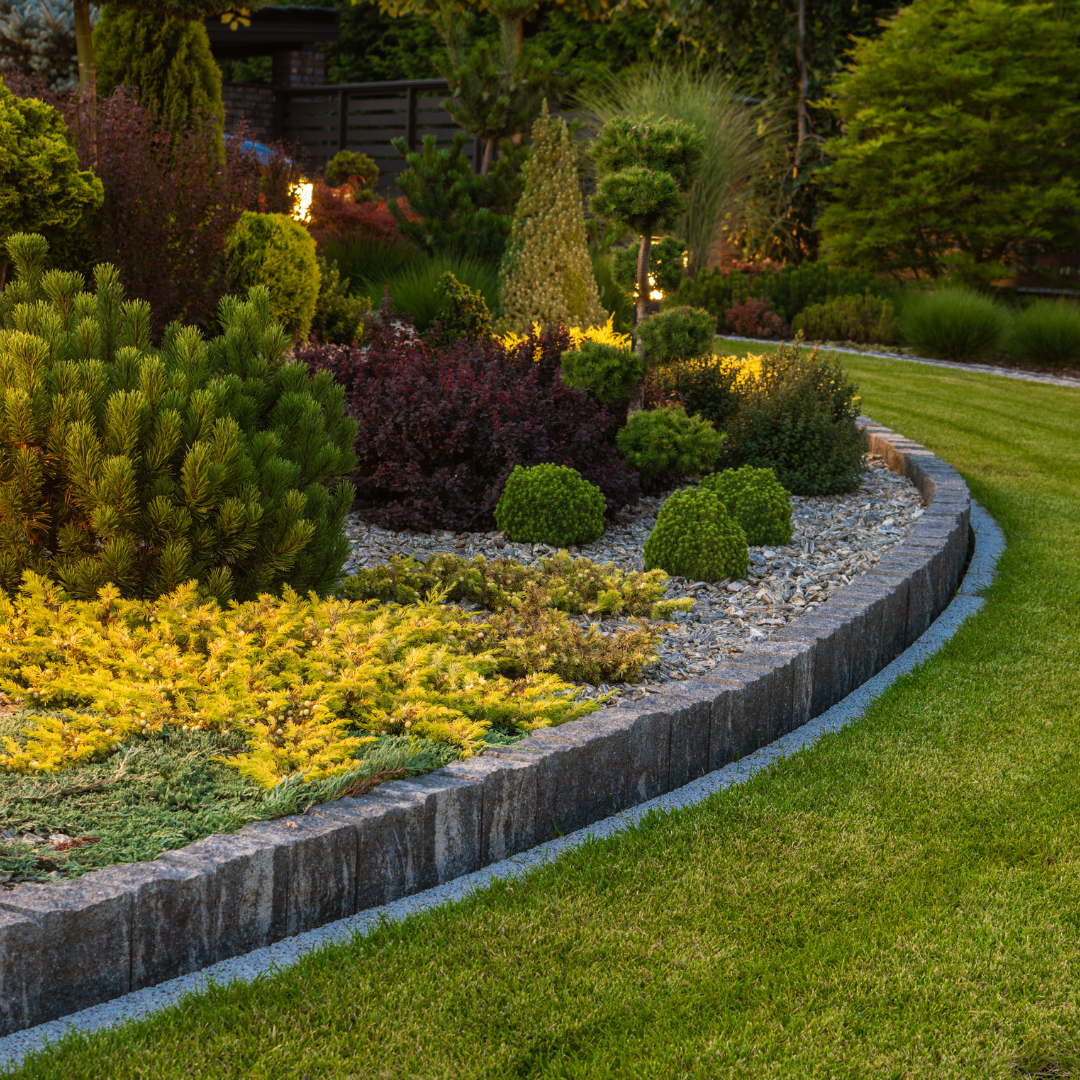 A lush garden with various colorful plants and a neatly trimmed lawn bordered by a stone wall.