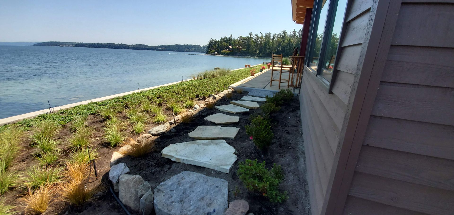 Laying sod in a garden. Rolls of turf sit beside a rake on prepared soil, next to a stone path.