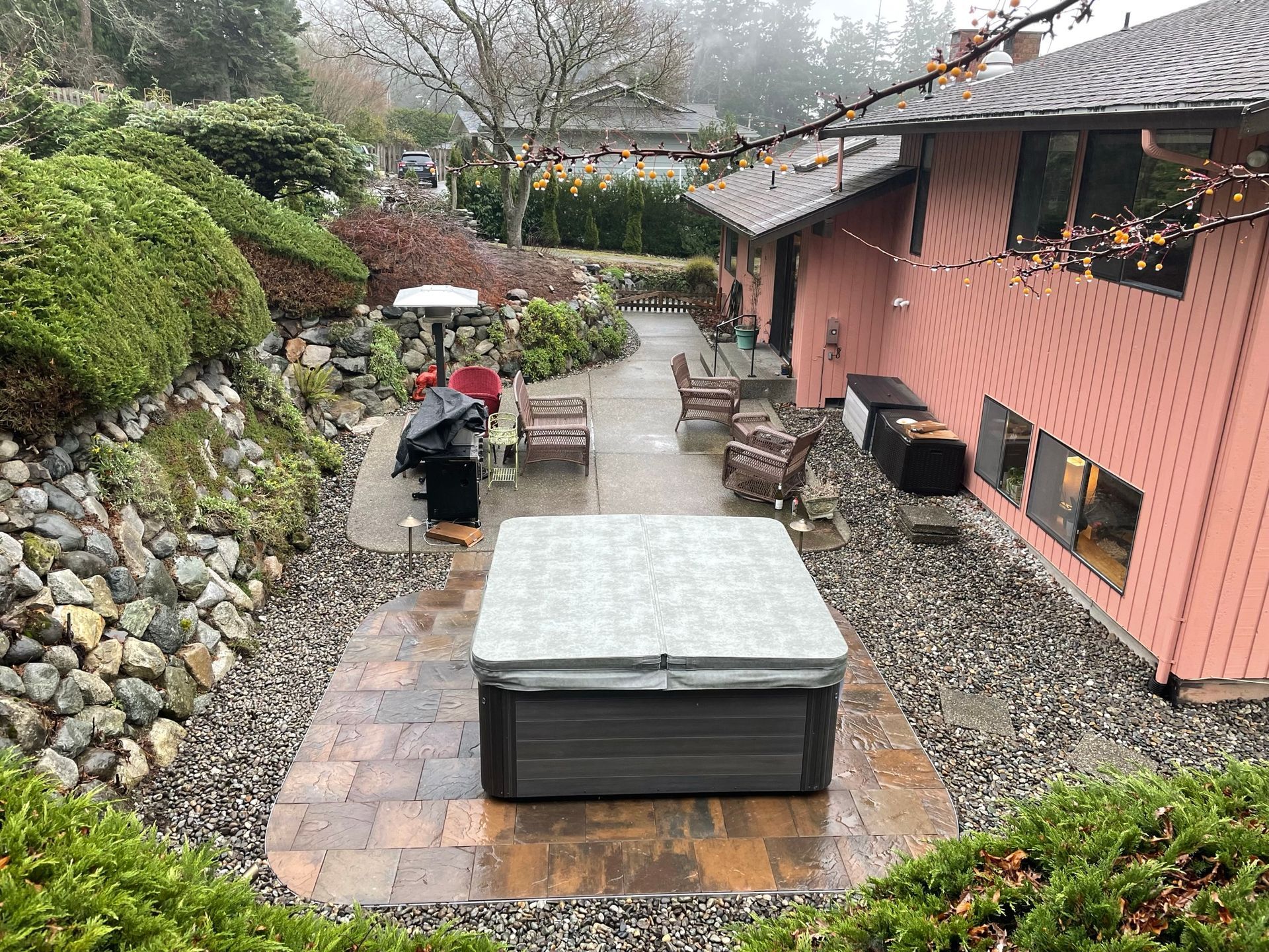 Backyard patio with hot tub, chairs, and pink house. Overcast day with low visibility.