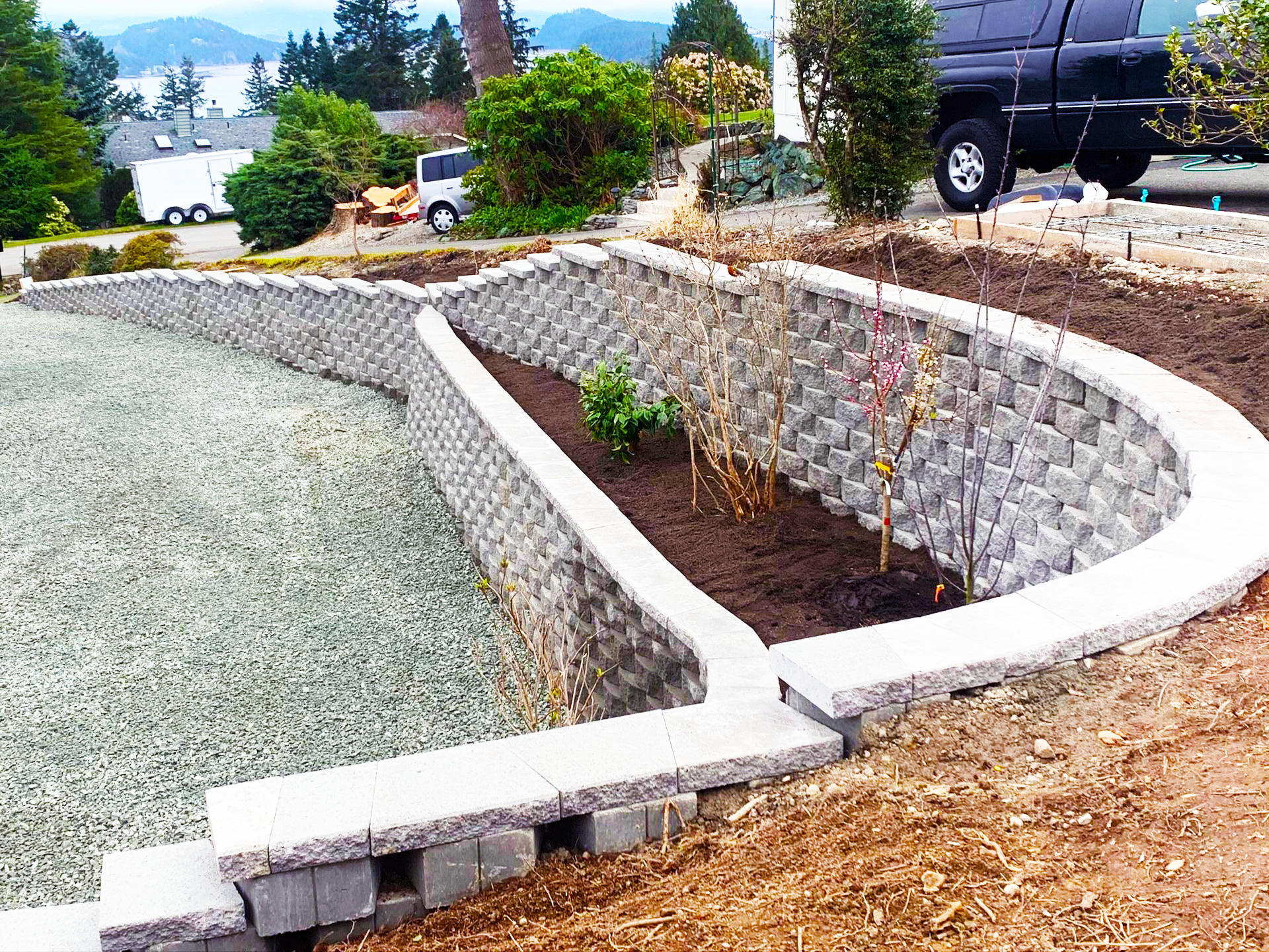 Curved retaining walls with gray blocks and concrete, surrounding gravel and planting beds.