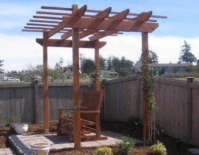 Wooden pergola with a chair inside in a backyard setting.