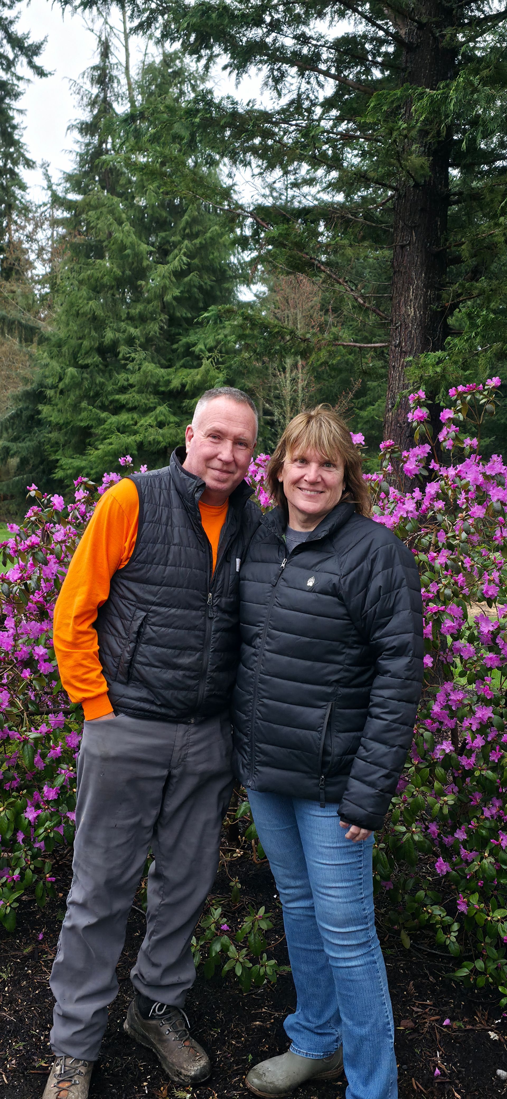 Man in orange hoodie and woman by lawn tractor.