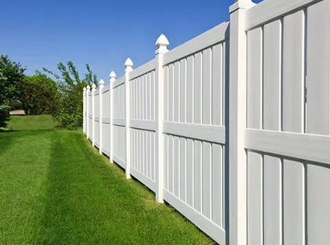 White vinyl fence along green lawn under a blue sky.