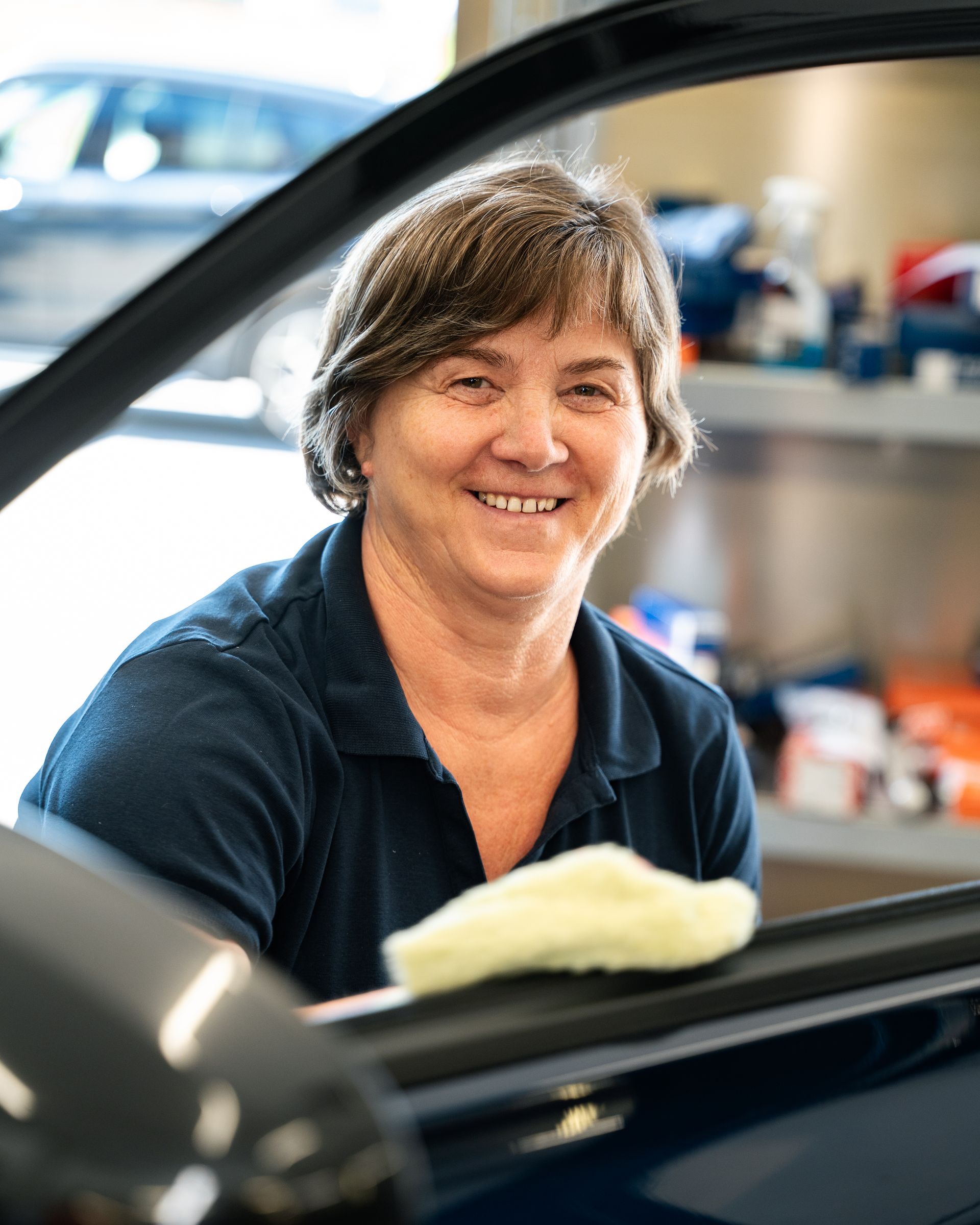 Eine Frau in einem blauen Hemd steht mit verschränkten Armen vor einem Auto.