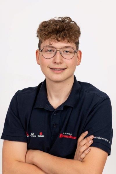 Ein junger Mann mit Brille und blauem Hemd steht mit verschränkten Armen da.