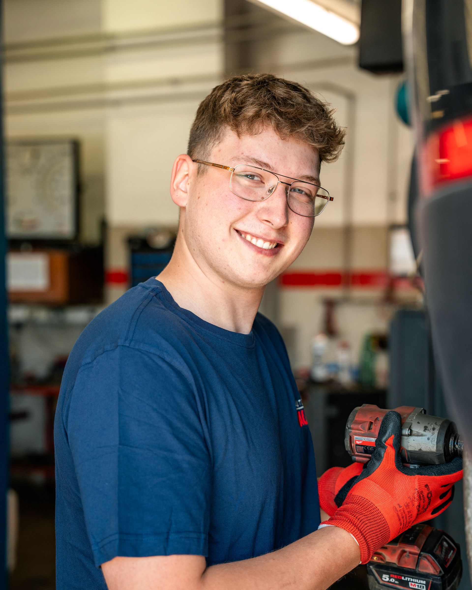 Ein junger Mann mit Brille und blauem Hemd steht mit verschränkten Armen da.