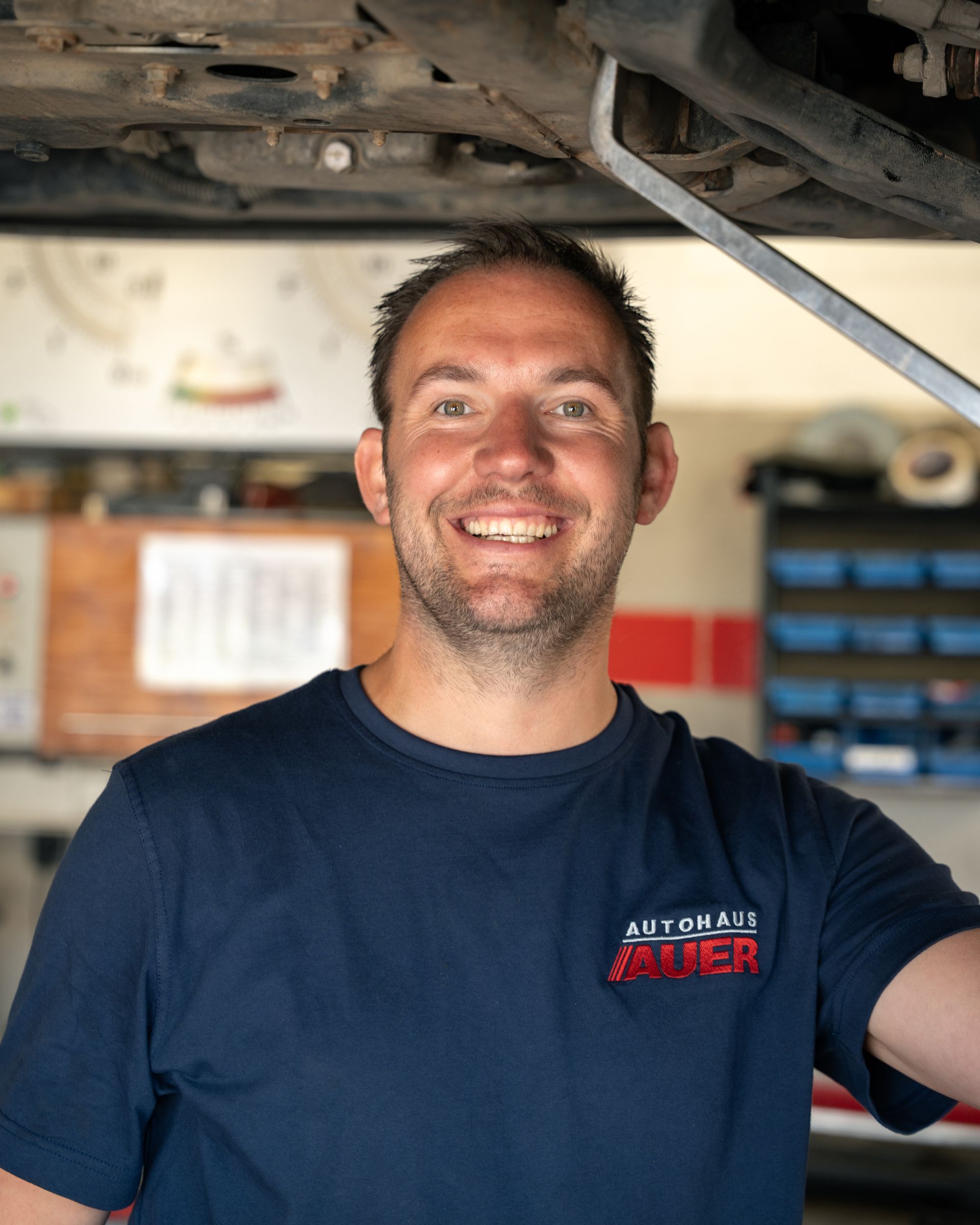 Ein junger Mann in einem blauen Hemd steht mit verschränkten Armen vor einem Auto.