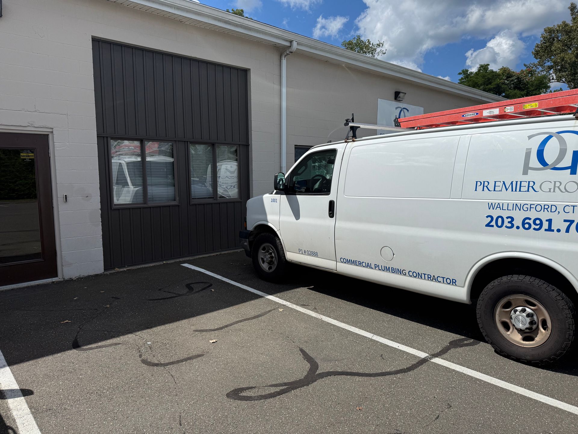 White van parked in front of a gray building with a Premier Group logo and ladder on top.
