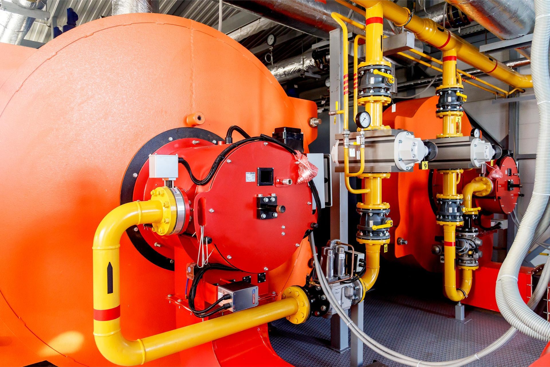 Orange industrial boiler with yellow pipes and valves, indoor setting.