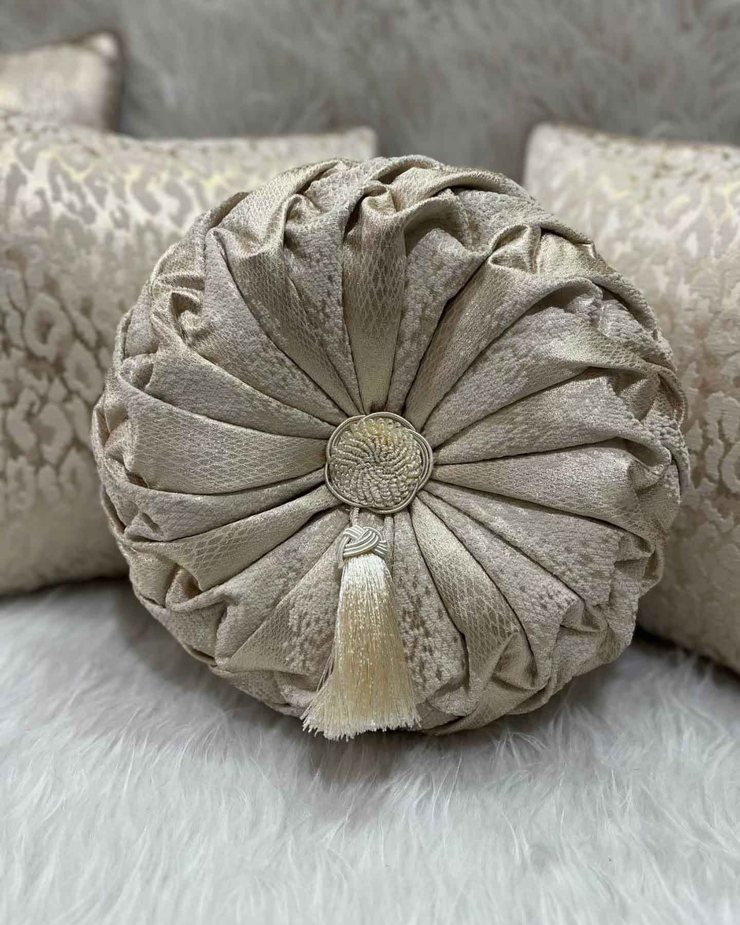 A round pillow with a tassel is sitting on a couch next to other pillows.