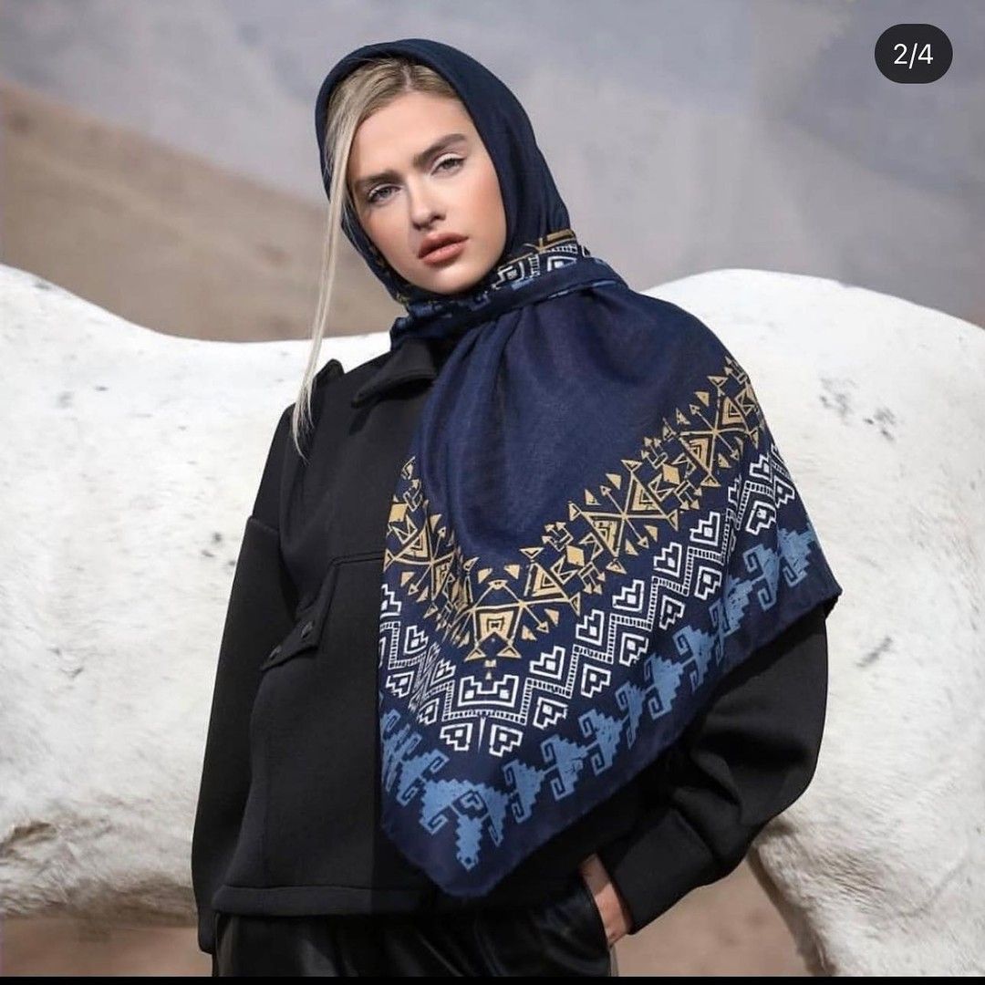 A woman wearing a hooded scarf is standing next to a white horse.