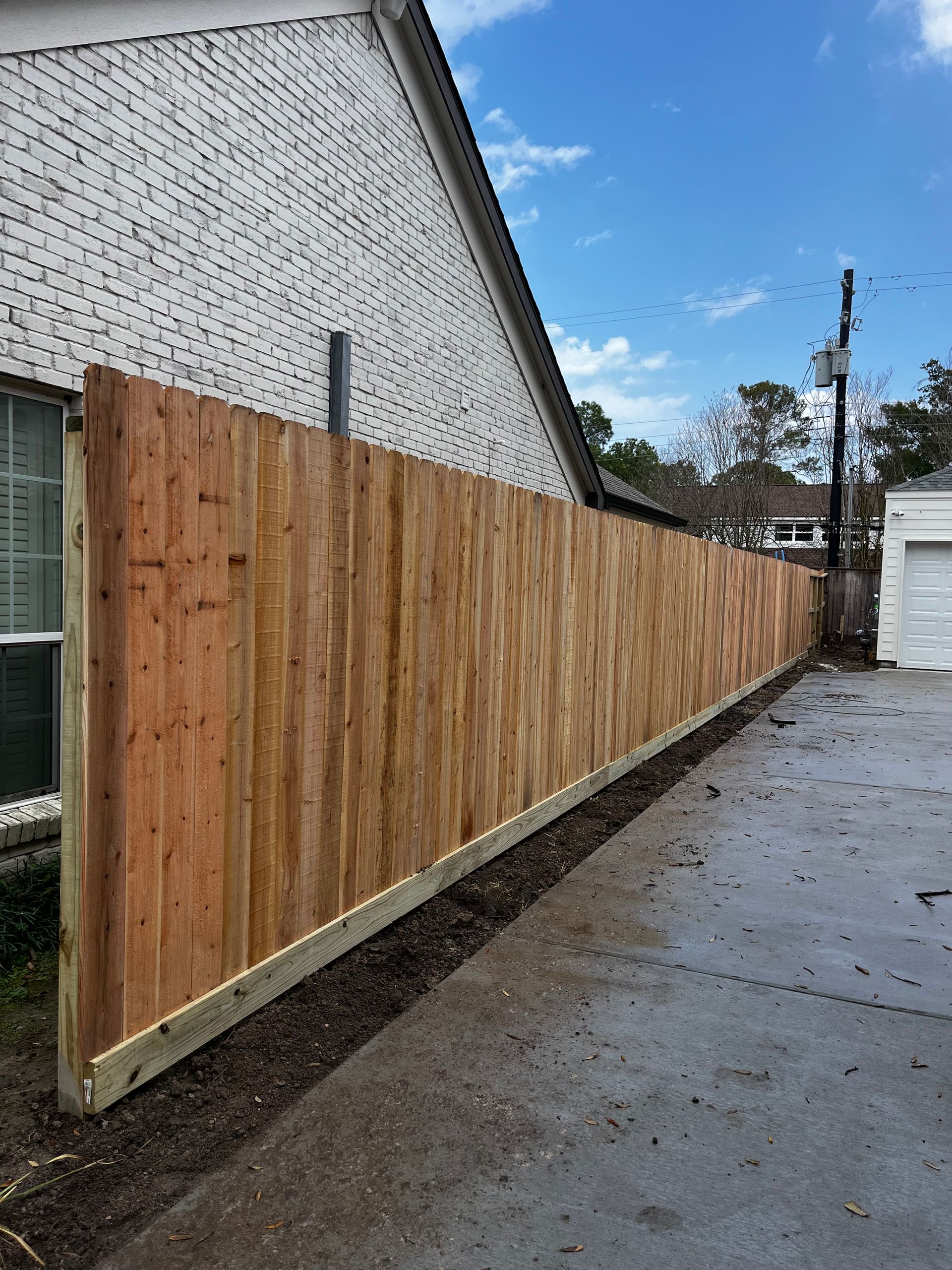 A wooden fence is sitting on the side of a driveway next to a house.