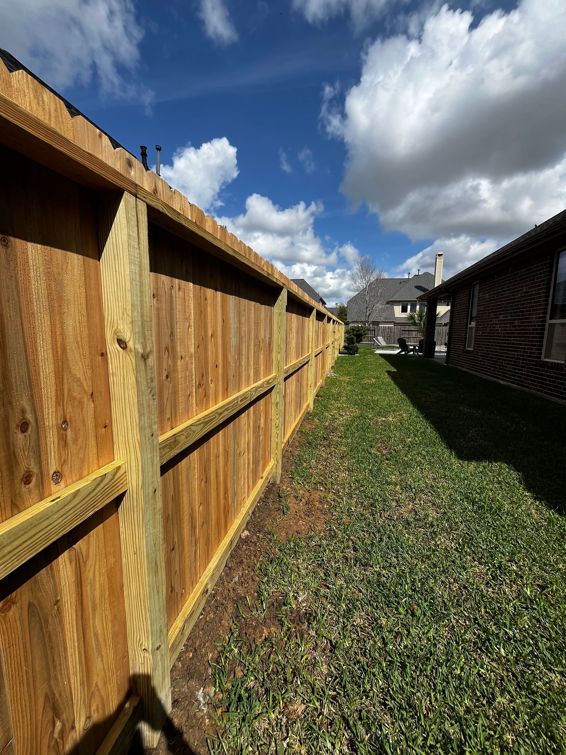 A wooden fence surrounds a lush green yard in front of a house.