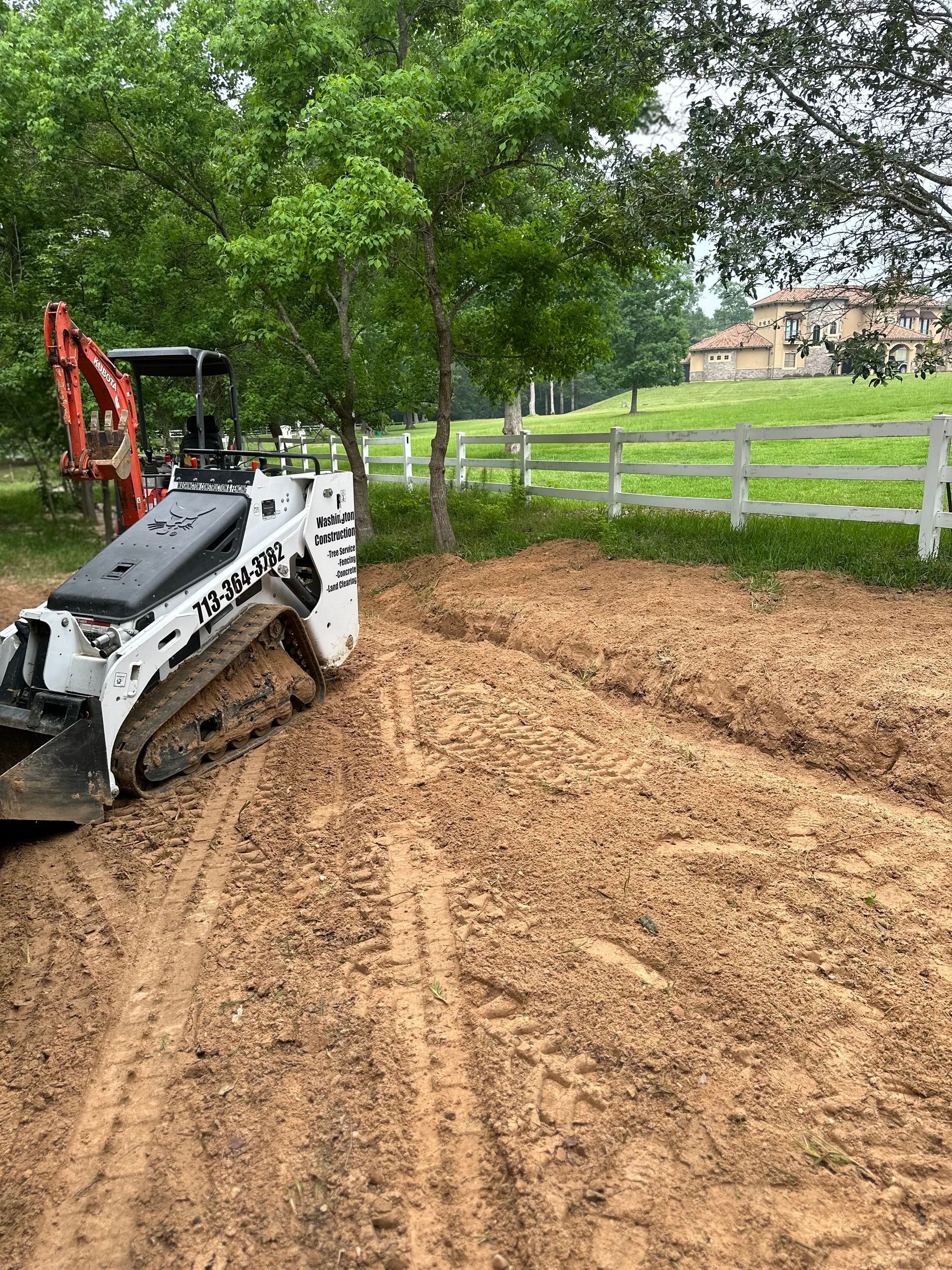 A bulldozer is sitting on top of a dirt field next to a fence.