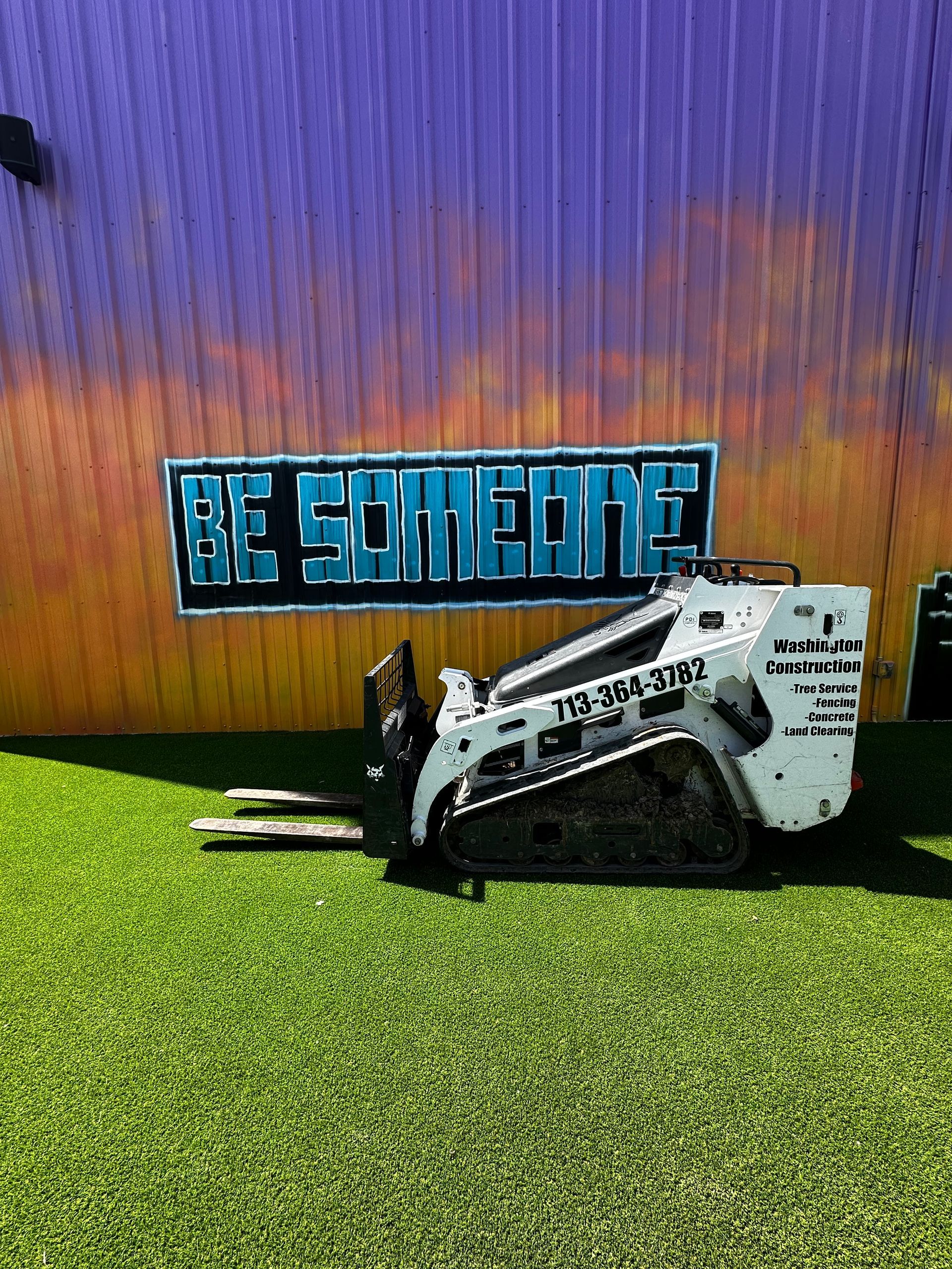 A forklift is parked in front of a building with a sign that says `` be someone ''.