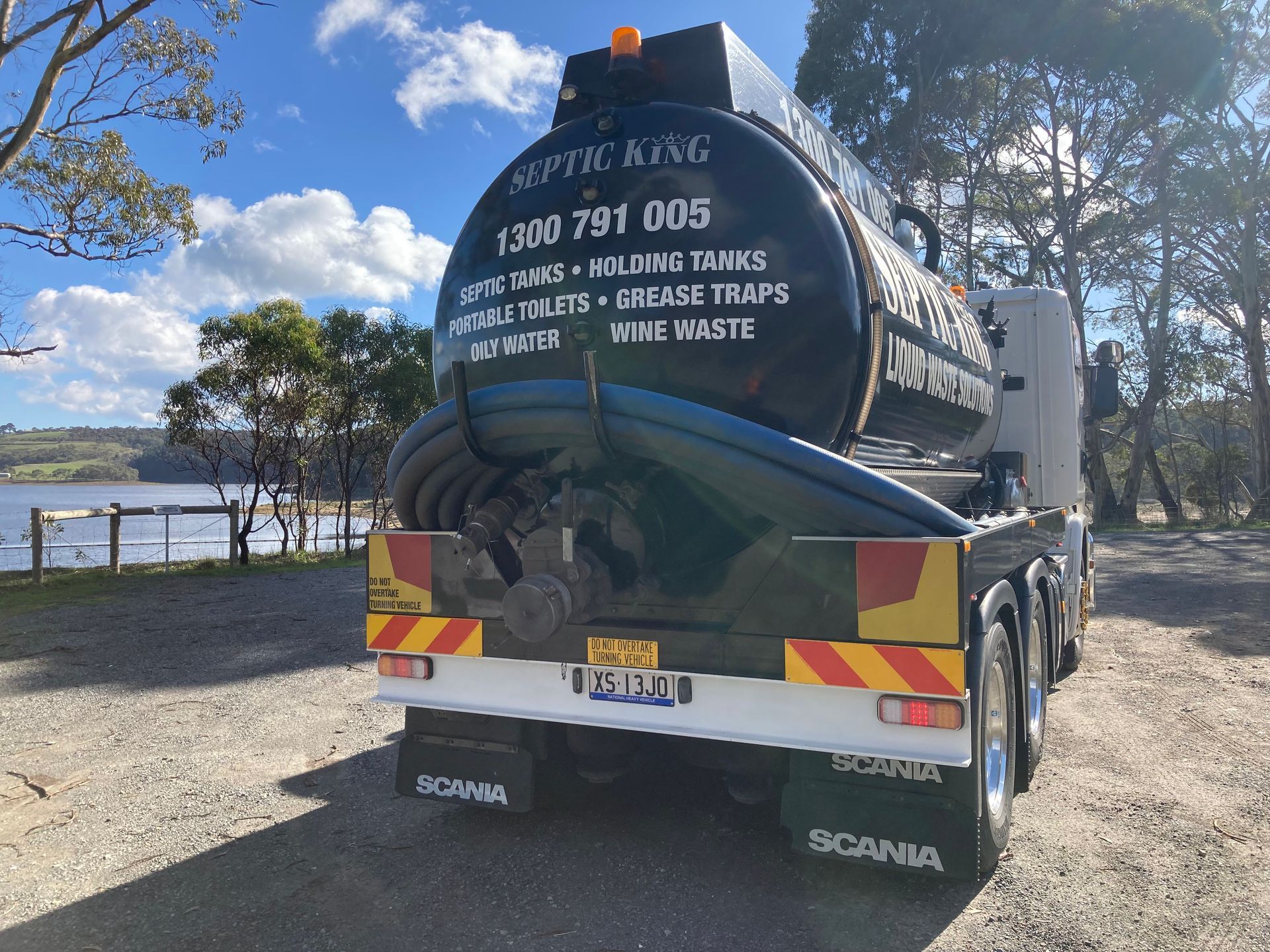 A person in blue work-wear is using a hose to empty a septic tank.