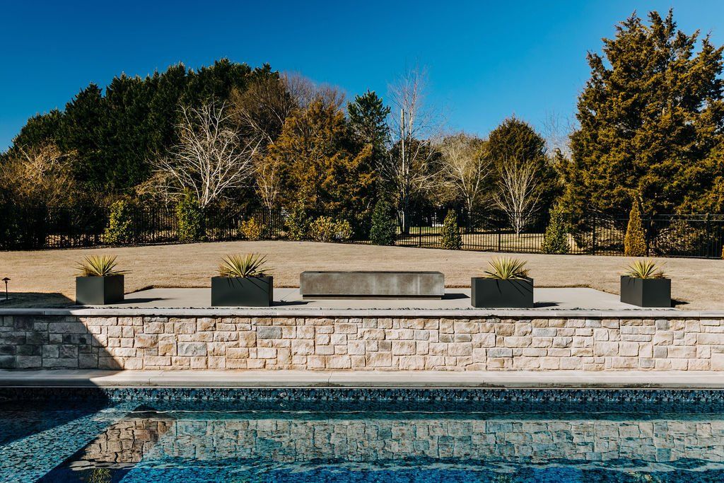 Stone retaining wall next to pool with modern rectangular pots and firepit.