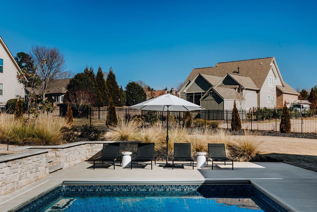 Black lounge chairs with umbrella on pool deck. Ornamental grasses.
