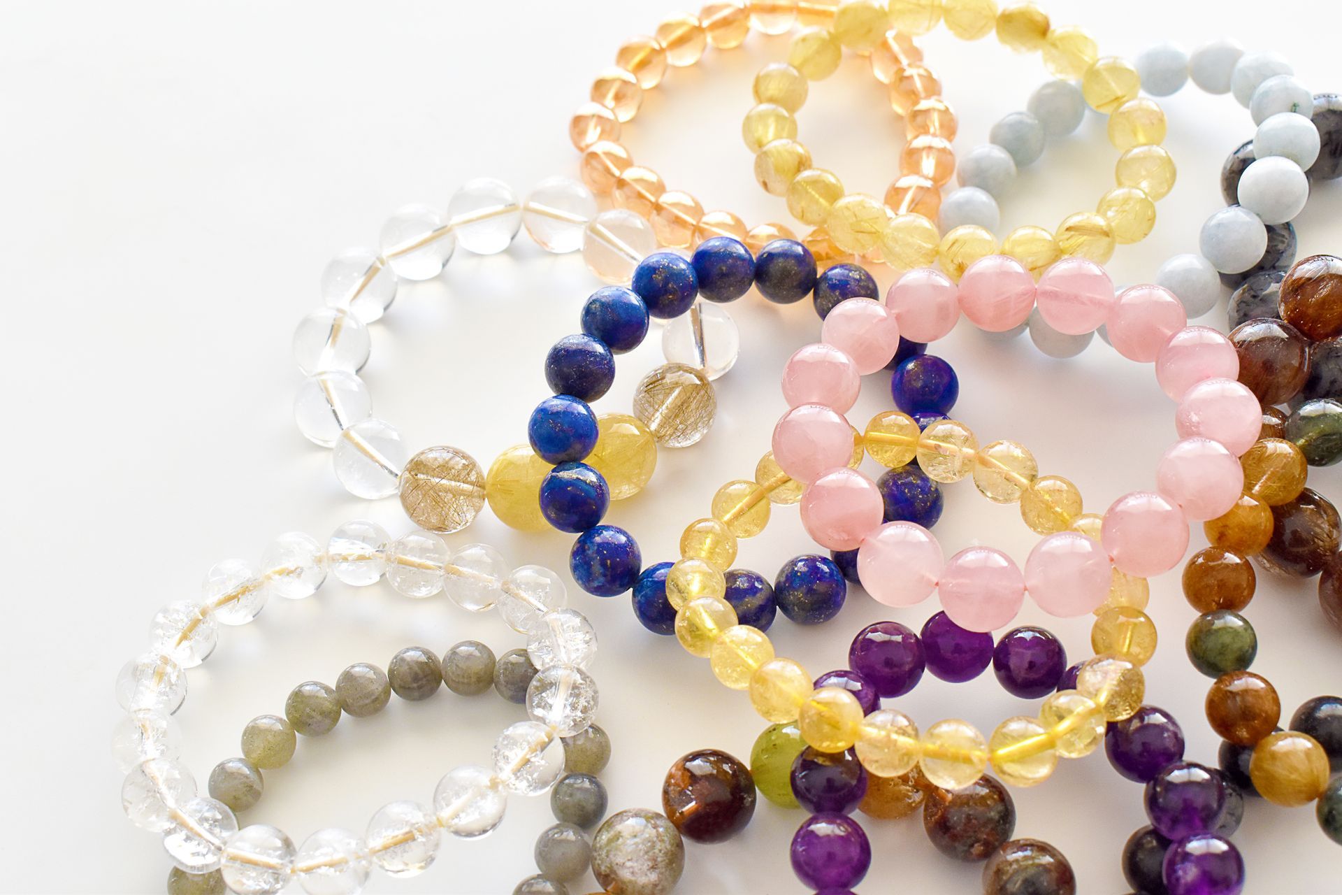 Pile of colorful beaded bracelets on a white surface, various crystal types and colors.