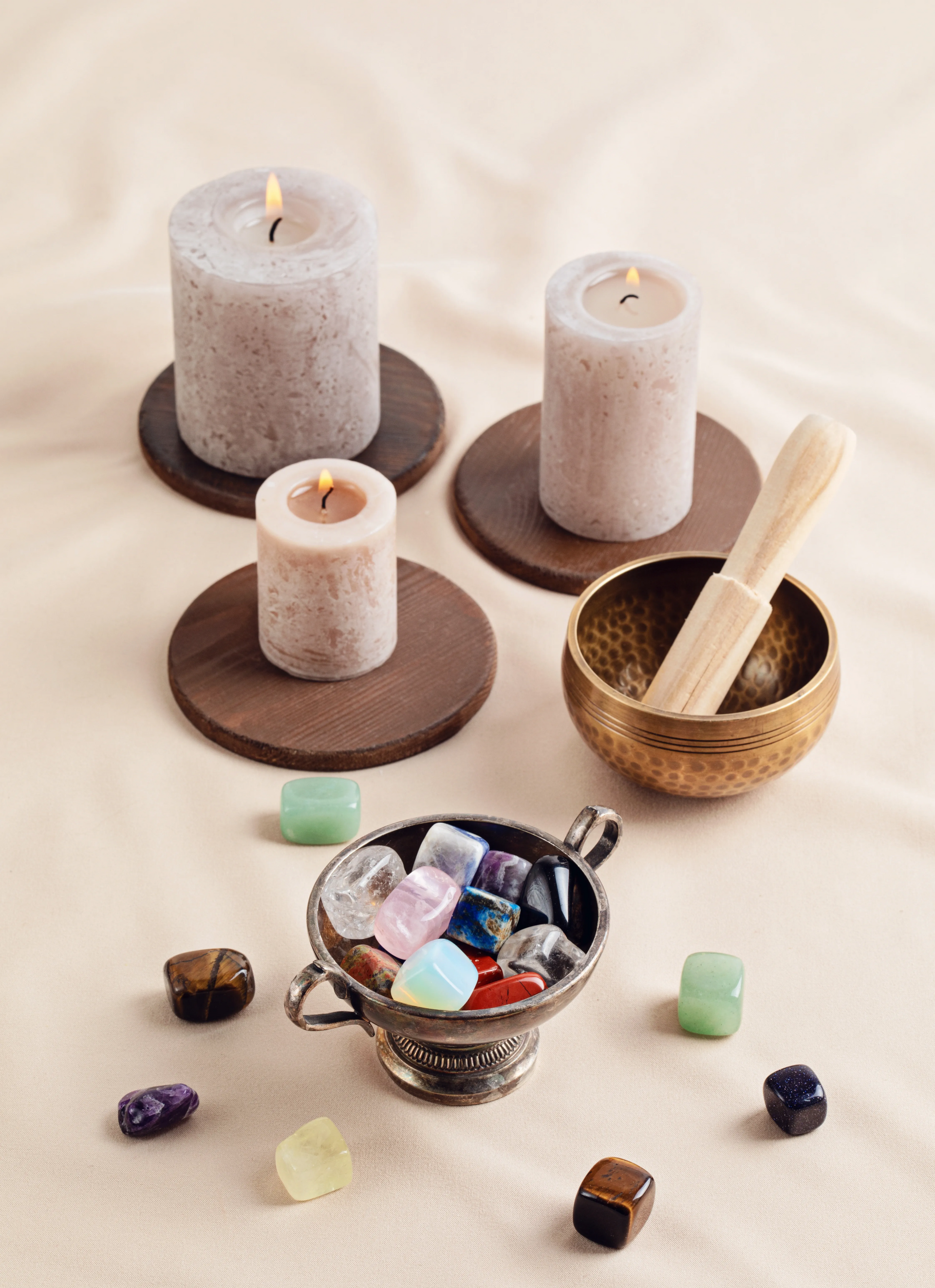 Candles, crystals, and a singing bowl on a cream-colored cloth, promoting relaxation.