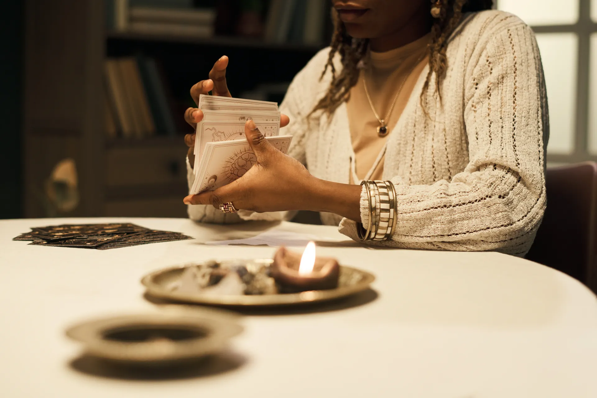 Woman holding jar of seeds, lit candle and seeds on table.
