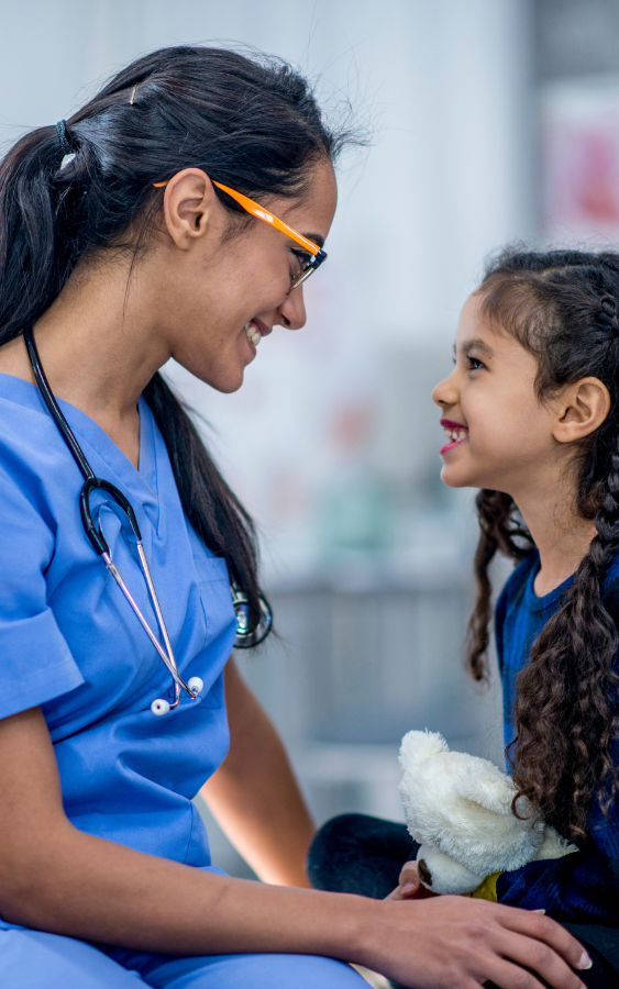 A nurse is talking to a little girl who is holding a teddy bear.