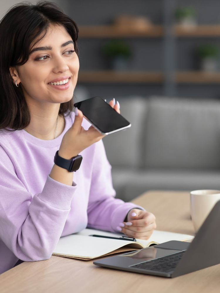 A woman is sitting at a table with a laptop and a cell phone.