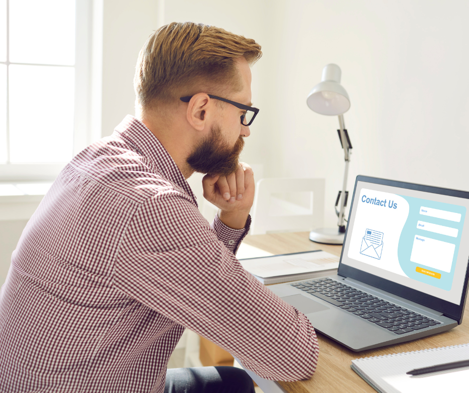 A man is sitting at a desk looking at a laptop computer.