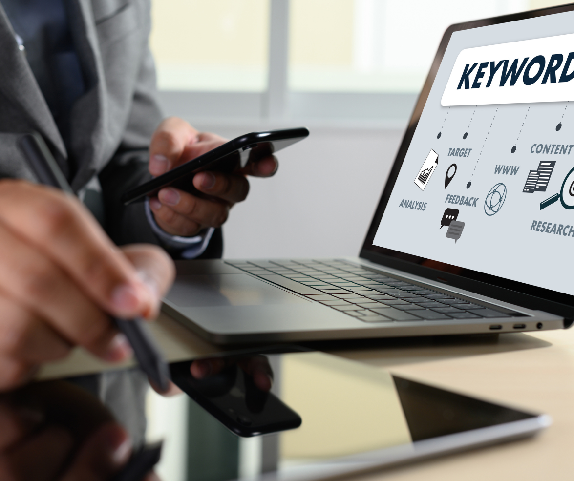 A man is holding a cell phone in front of a laptop that says keywords