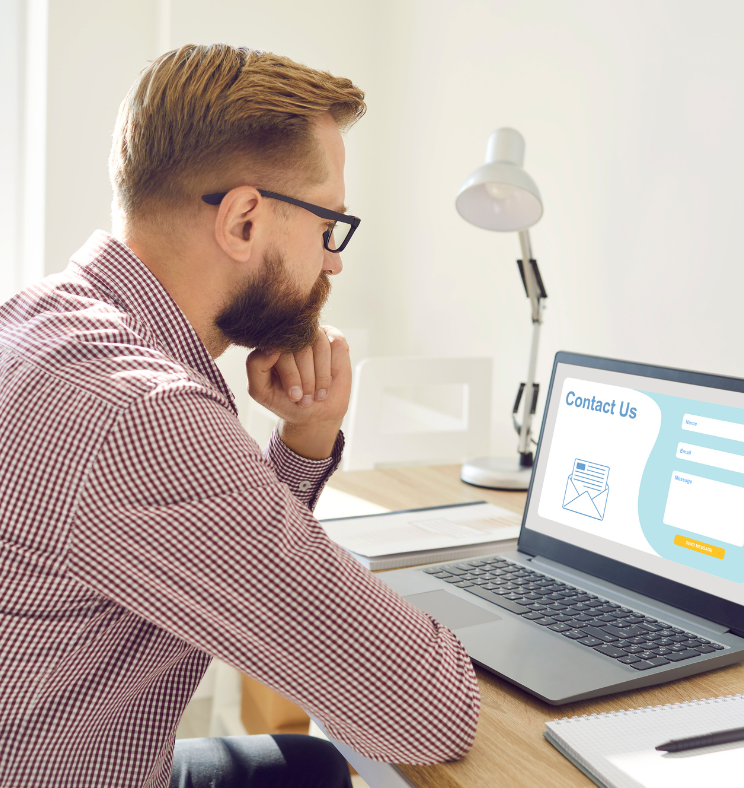 A man is sitting at a desk looking at a laptop computer.