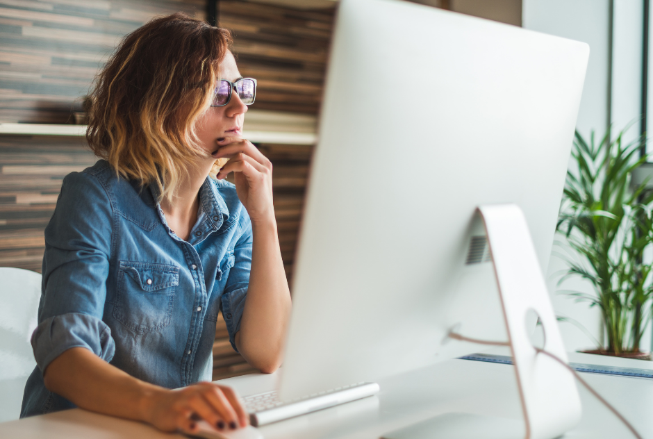 A woman is sitting at a desk looking at a computer screen.