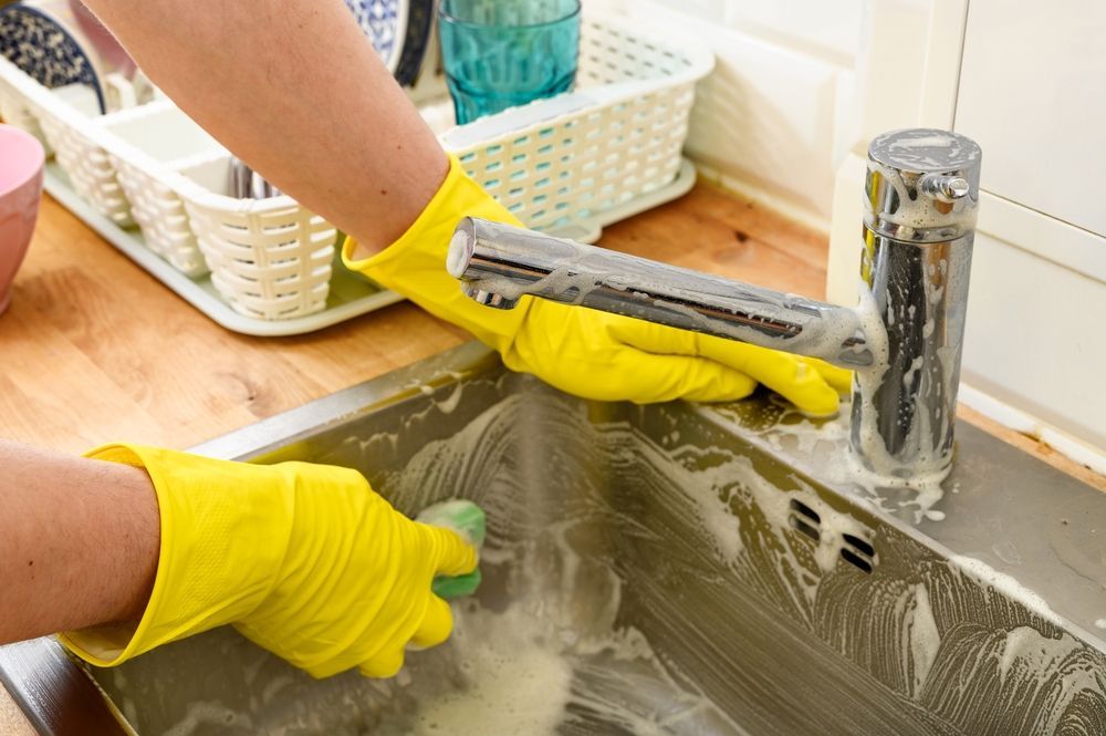 A person wearing yellow gloves is cleaning a sink with a sponge.