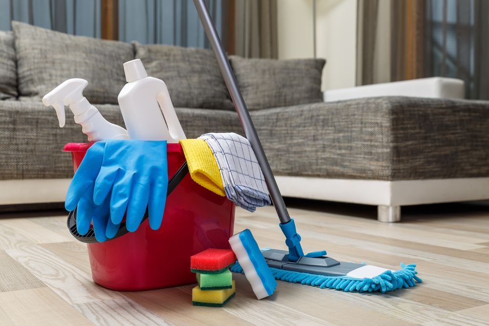 A red bucket filled with cleaning supplies and a mop in a living room.