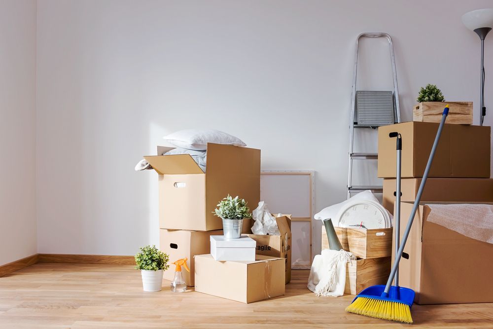 A room filled with cardboard boxes , a broom and a ladder.