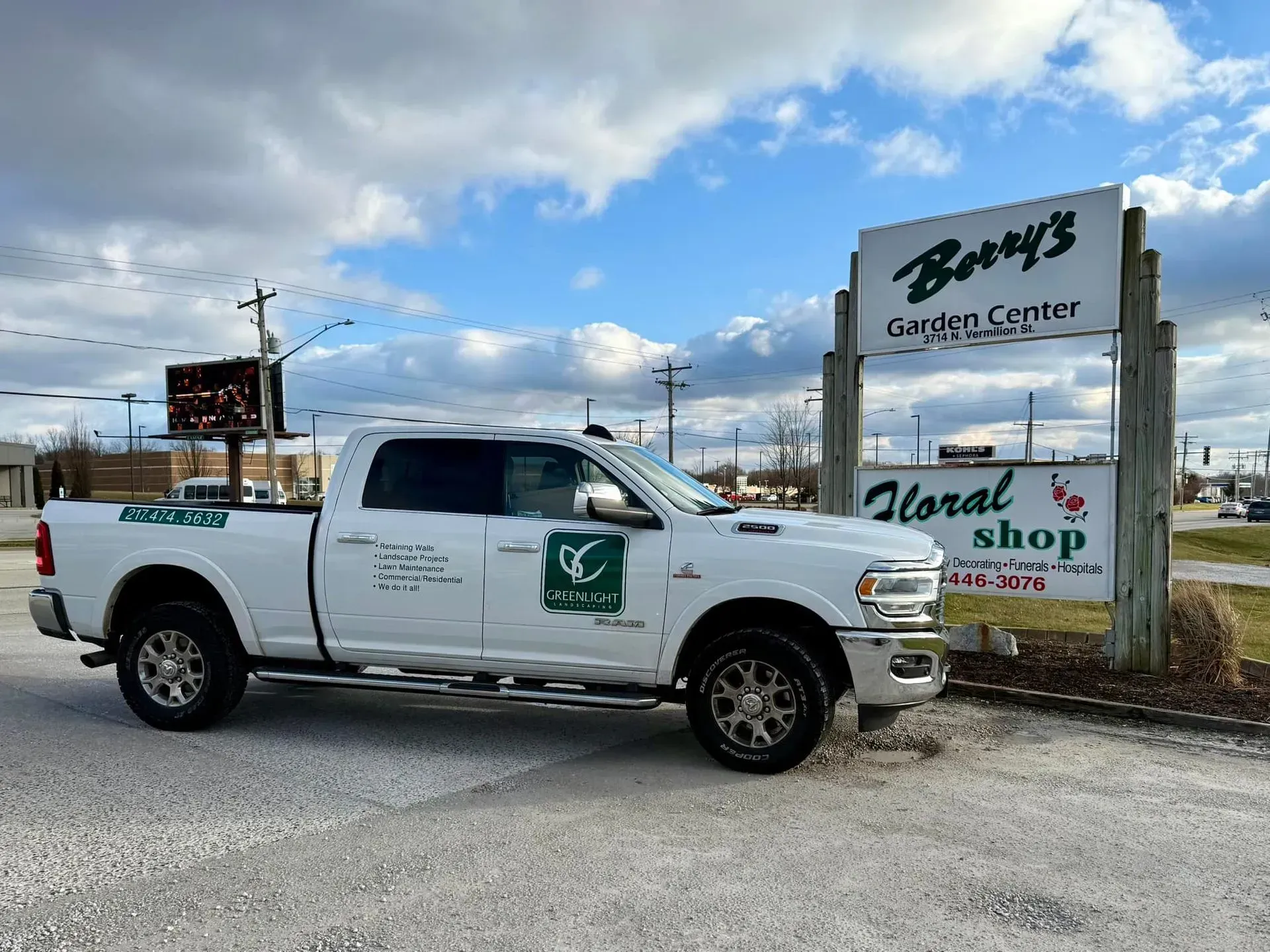White truck with company logo parked outside Barry's Garden Center & Floral Shop sign under a cloudy sky.