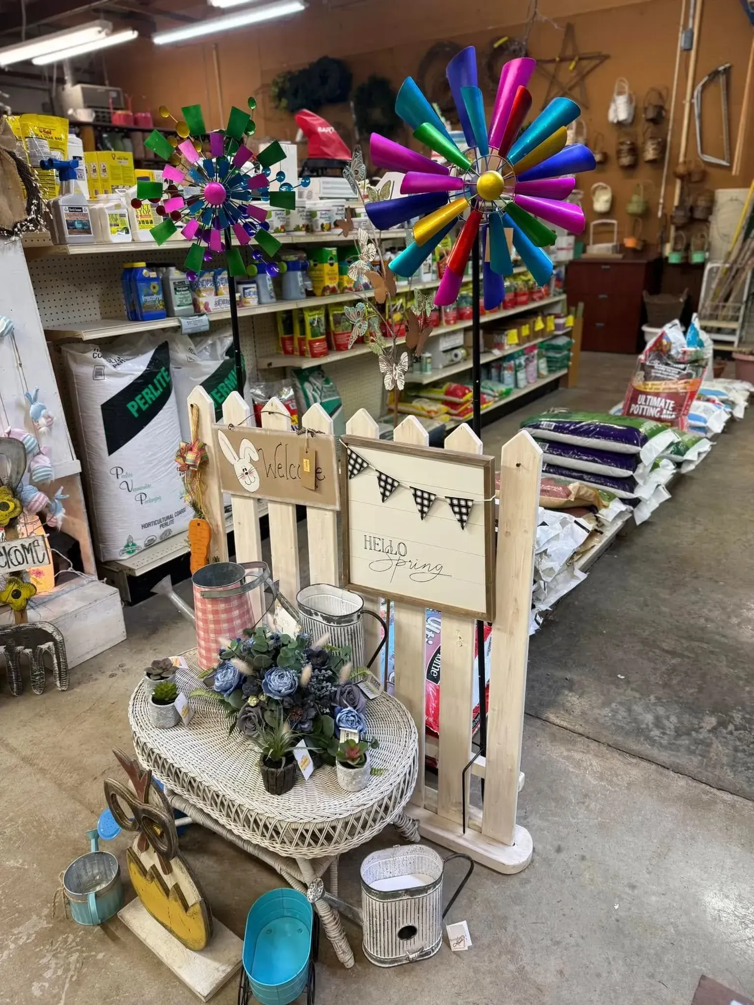 A garden center display with a white picket fence, windmill decor, and shelves of gardening supplies. A garden center display with a white picket fence, windmill decor, and shelves of gardening supplies.