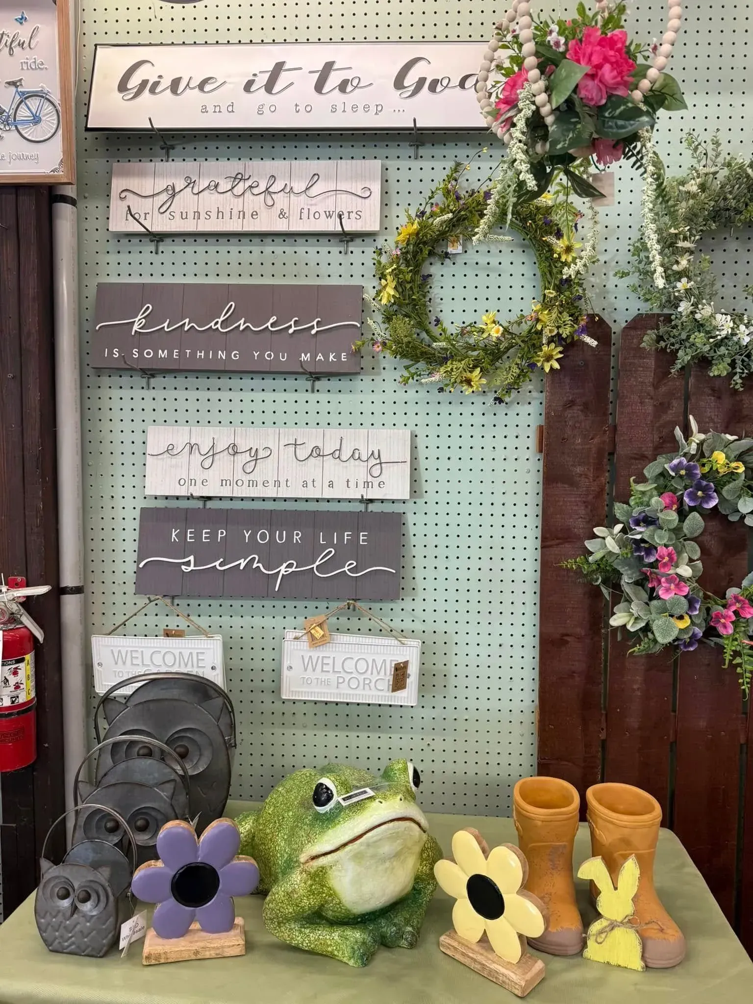Display of inspirational signs, wreaths, and garden decor including a frog, owl, and boots. Display of inspirational signs, wreaths, and garden decor including a frog, owl, and boots.