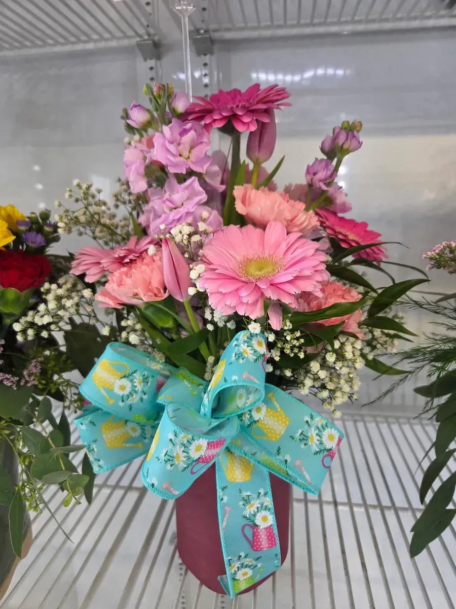 Floral arrangement in a maroon vase with pink gerbera daisies and a blue bow.