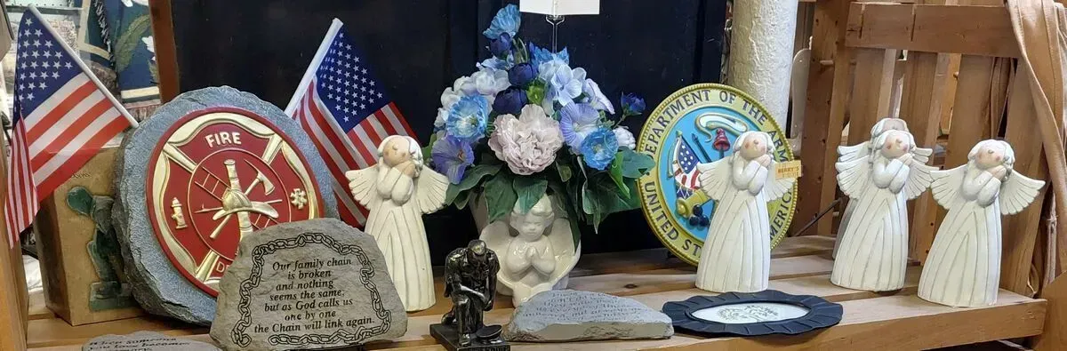 Shelf display with American flags, firefighter emblem, angels, and flowers.