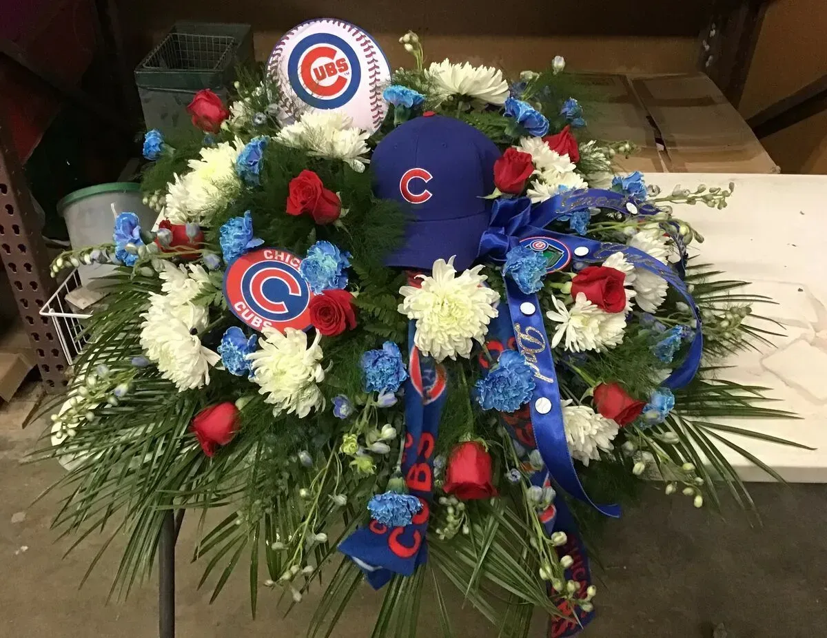 Floral arrangement with Chicago Cubs baseball theme: white and blue flowers, red roses, cap, and baseball.